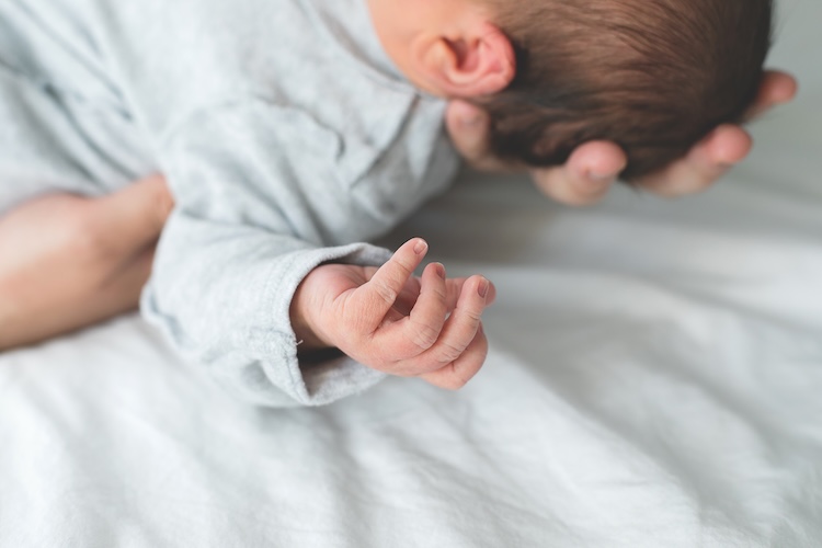 Newborn Baby In Cocon On Bed. Lifestyle, Family Life Concept. Hand With Fingers Of A Newborn Baby Newborn Baby In Cocon On Bed. Lifestyle, Family Life Concept. Hand With Fingers Of A Newborn Baby
